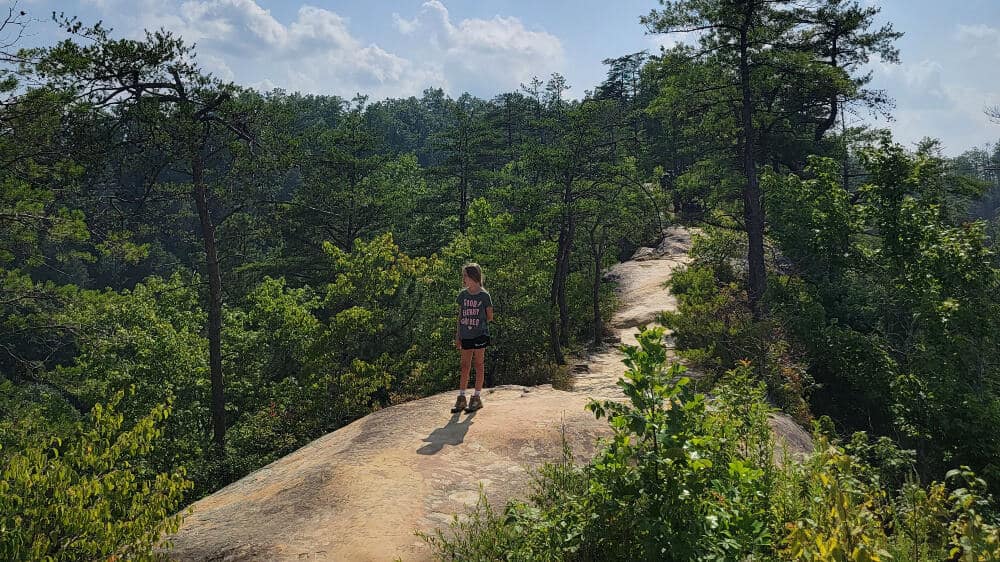 a young girl walks on top of a natural stone arch in red river gorge