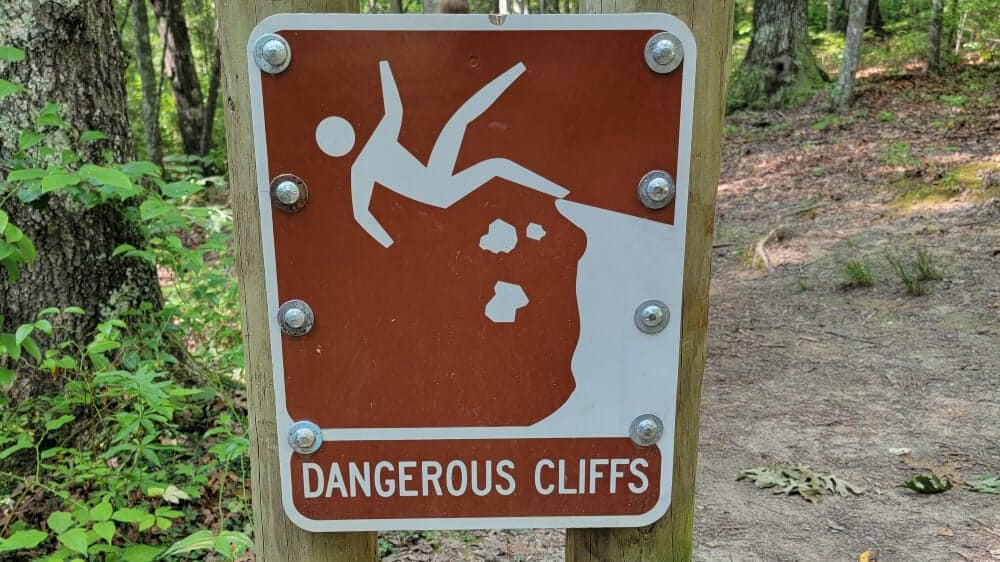 Sign that reads "dangerous cliffs" and shows a cartoon figure falling backward off a cliff