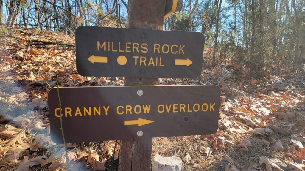 Two trail signs reading "Millers Rock Trail" with an arrow pointing to the left and "CRanny Crow Overlook" with an arrow pointing to the right