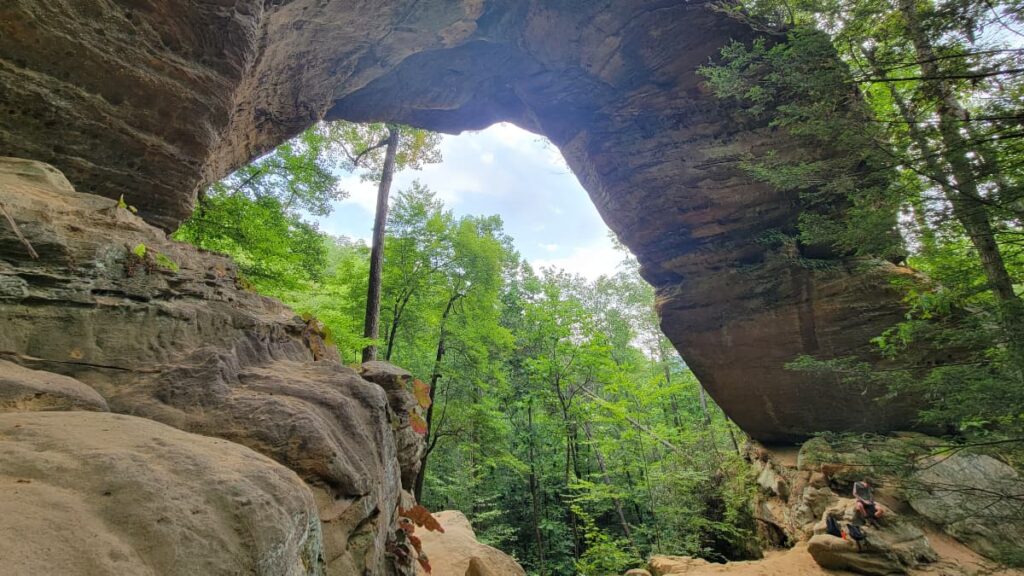 A boy sits below a massive stone arch at Red River Gorge in Kentucky 