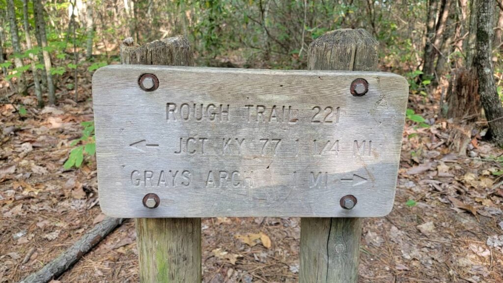 Trail sign that reads "Rough Trail 221" and "JCT KY 77  1 1/4 mi" with an arrow pointing to the left and "Grays Arch 1 mi" with an arrow pointing to the right