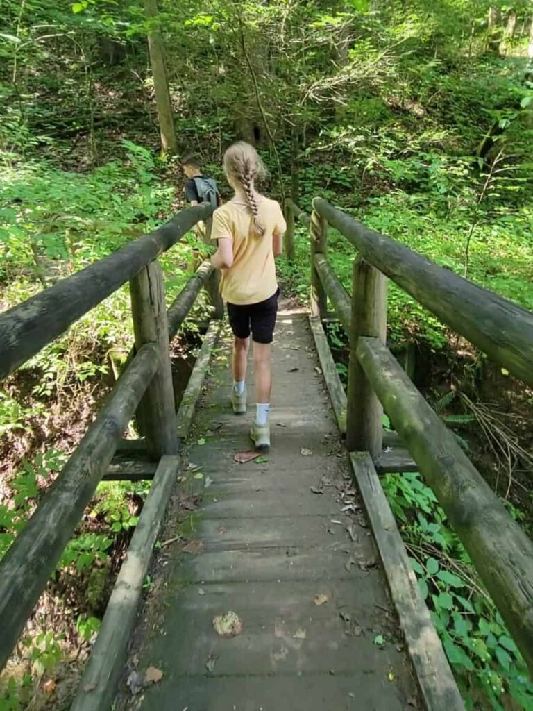 young girl crosses small wooden footbridge with wooden railings on either side
