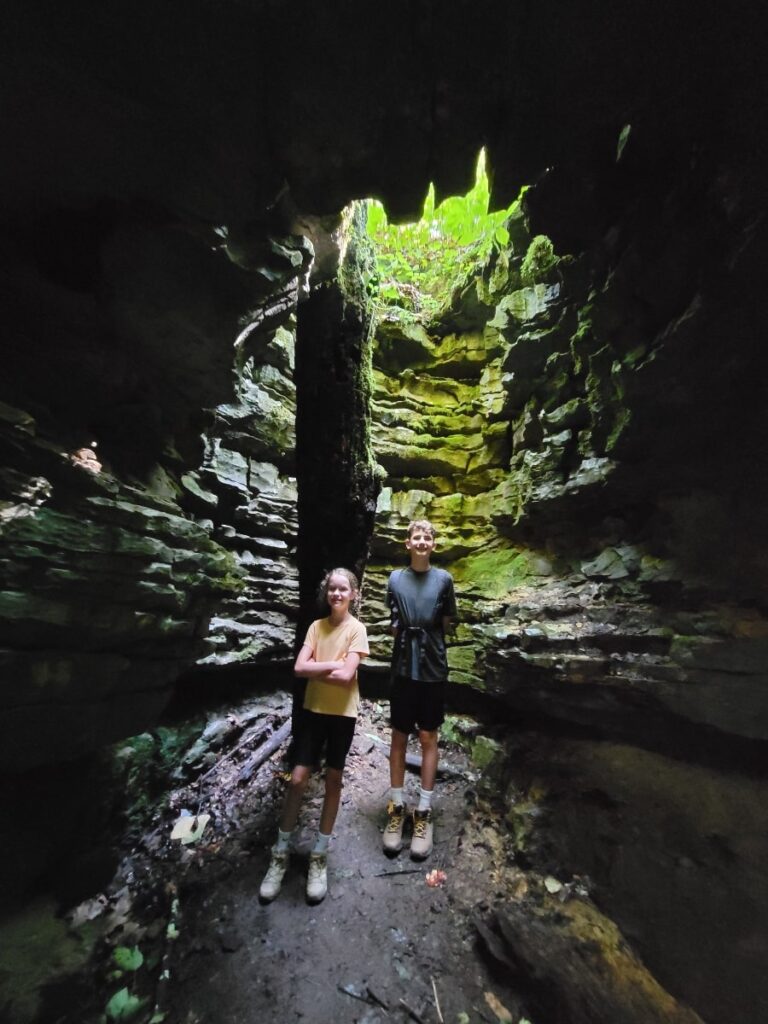 two kids stand inside a sinkhole with a stone arch above them