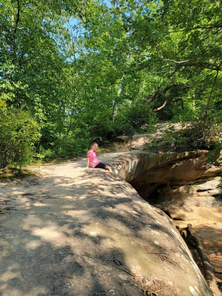 a young girl sits on top of a stone arch at red river gorge