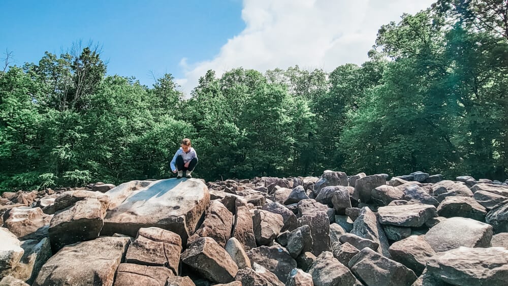 A young girl crouches down to hit a large boulder with a hammer at Ringing Rocks in Upper Black Eddy