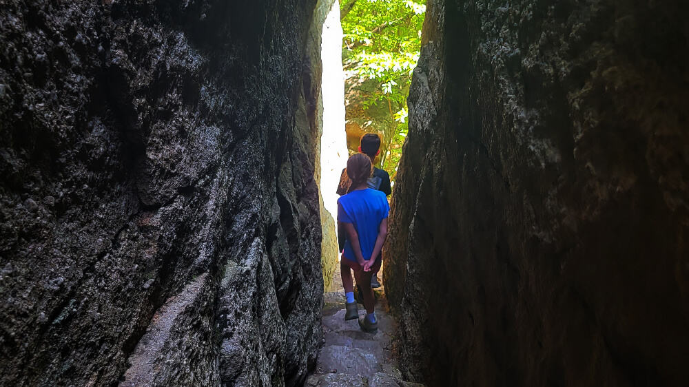 Twp children walk through a narrow pathway with large stones on either side