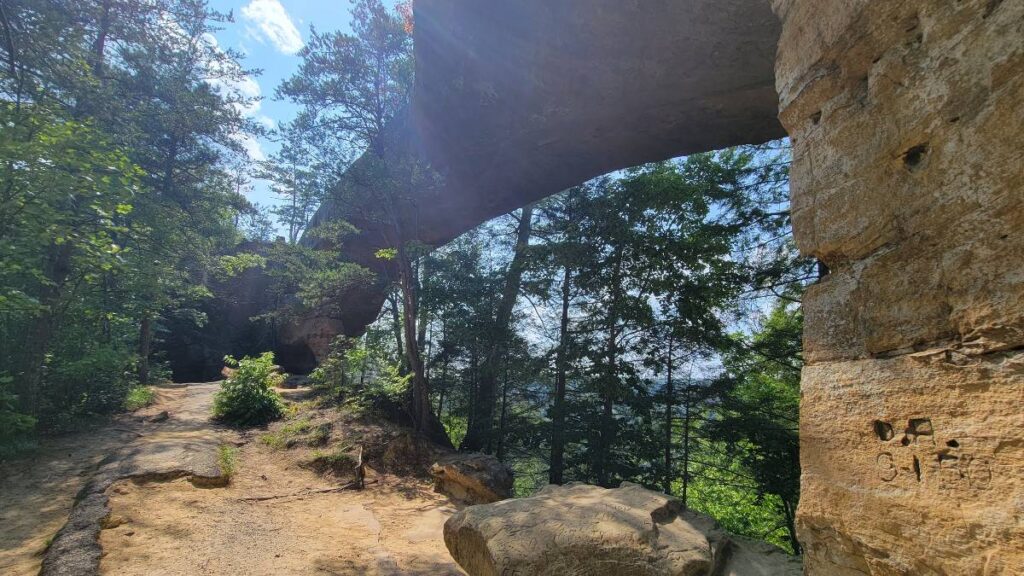 a large stone arch crosses over a path and large boulders below