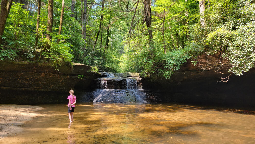 A young girl wades in the pool beneath a short waterfall