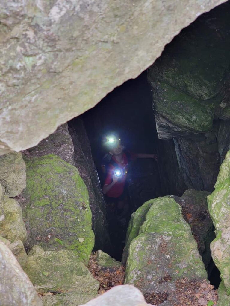 a young boy wearing a headlamp and using a flashlight looks up through a crevasse at the Pinnacle overlook