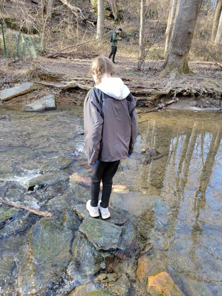 A young girl stands on a stone in the middle of a stream