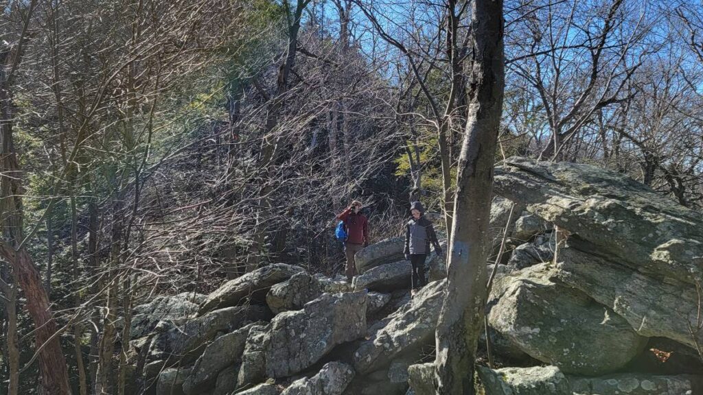 A father and daughter traverse over large rocks and boulders on the Hawk Mountain Skyline TRail