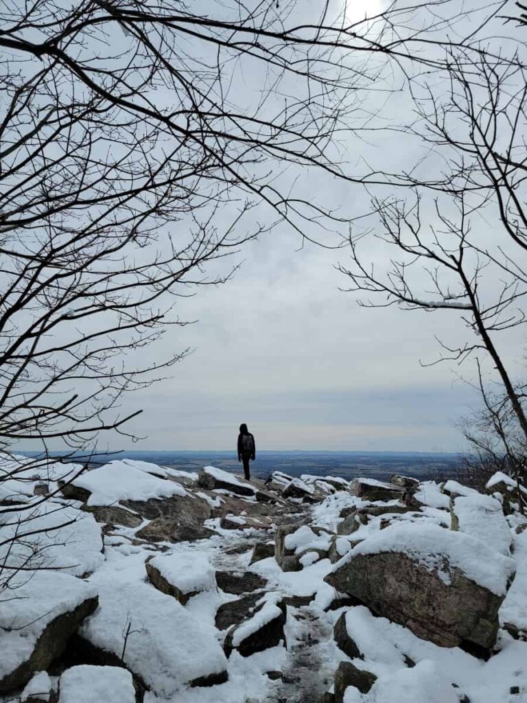 A boy stands on rocks in the distance with trees framing the shot. There is snow on the ground