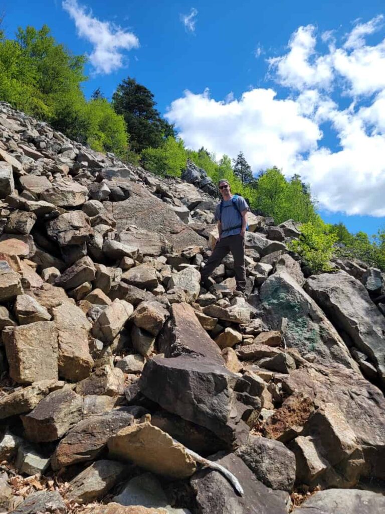 A man stands among large boulders on the side of a mountain