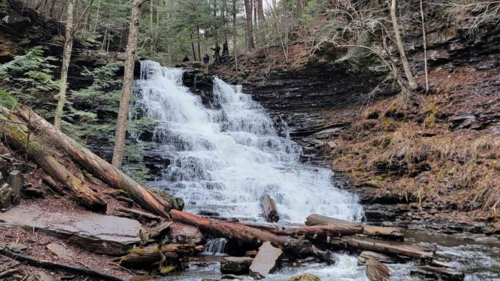 A tall waterfall with people standing at the top flows over rocks