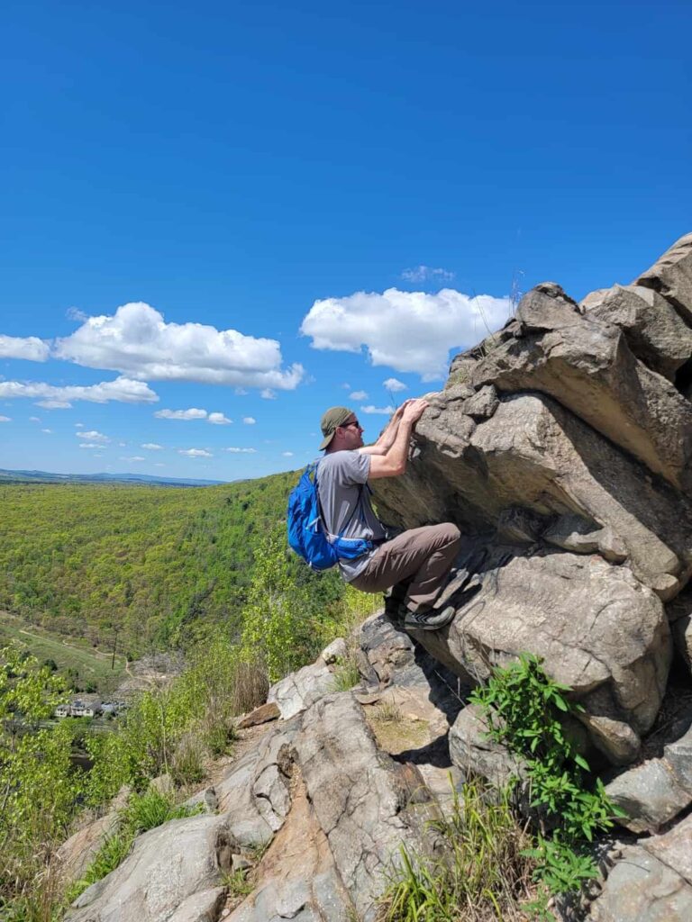 A man wearing a backpack clings to the face of a large boulder