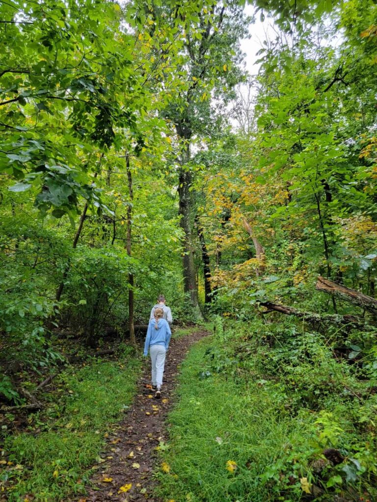 two kids walk along a flat dirt trail through the forest