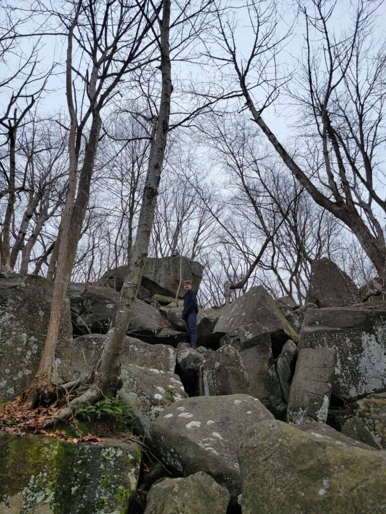 a boy stands on large boulder with several other large boulders below