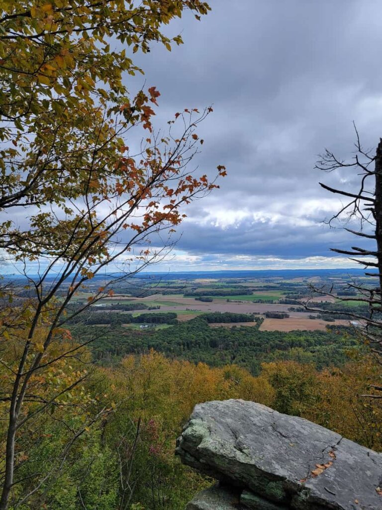 A view of a valley in the distance with a rock jutting out in the foreground during fall