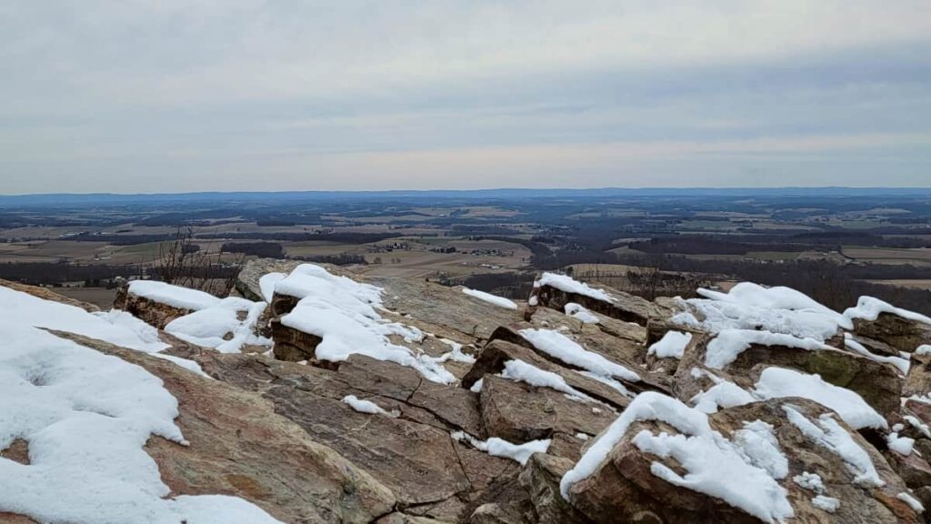 A view of the Lehigh Valley from Bake Oven Knob with rocks in the foreground. There is light snow on the ground.