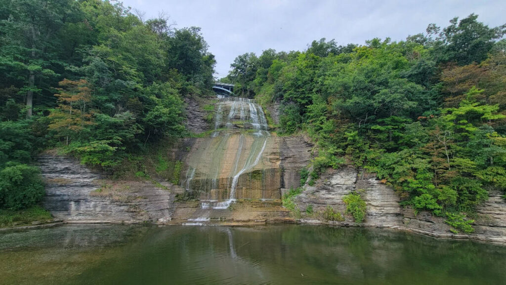 water cascades down a cliff into a pool while a road crosses over the top