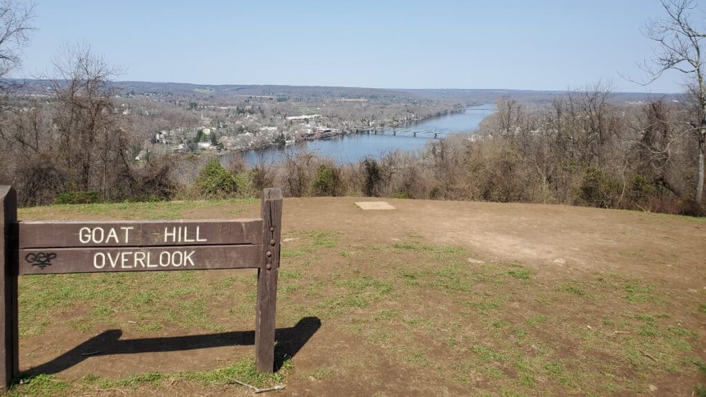 wooden sign in a large clearing overlooking a river reads "goat hill overlook"