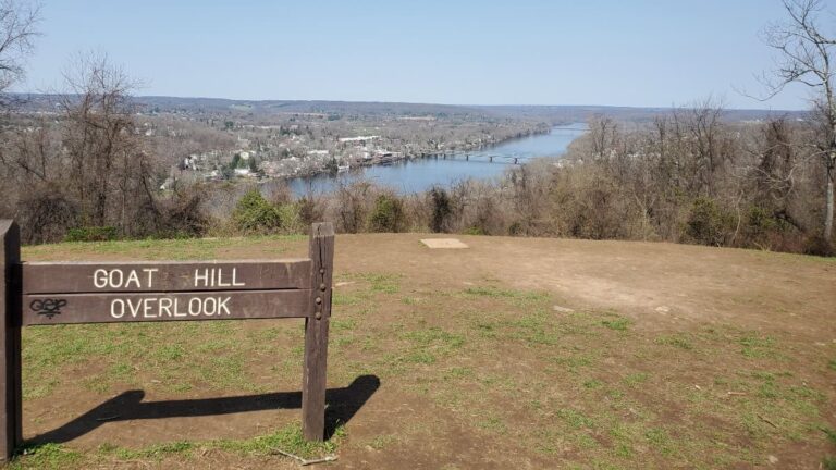 wooden sign in a large clearing overlooking a river reads "goat hill overlook"