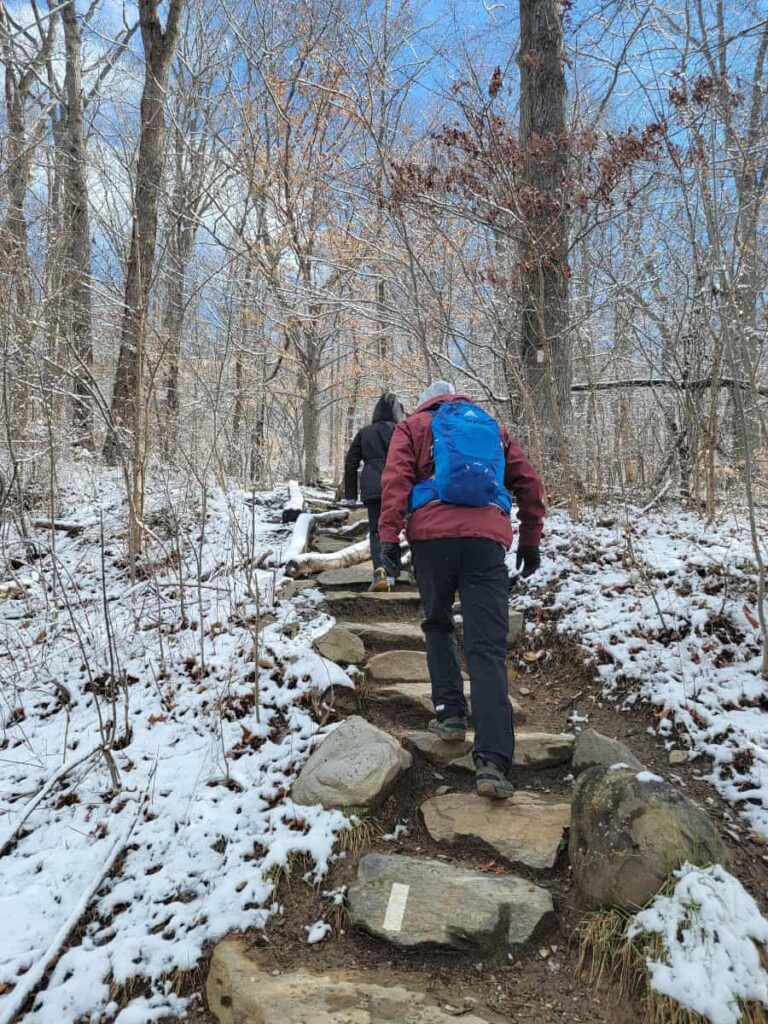 A man and two kids walk up stone steps on the Appalachian Trail at the start of the Weverton Cliffs hike