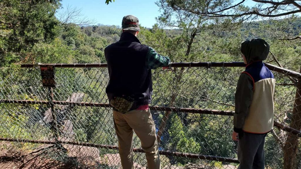 A man and young boy stand next to a fence as they look out over the Tohickon Creek at High Rocks