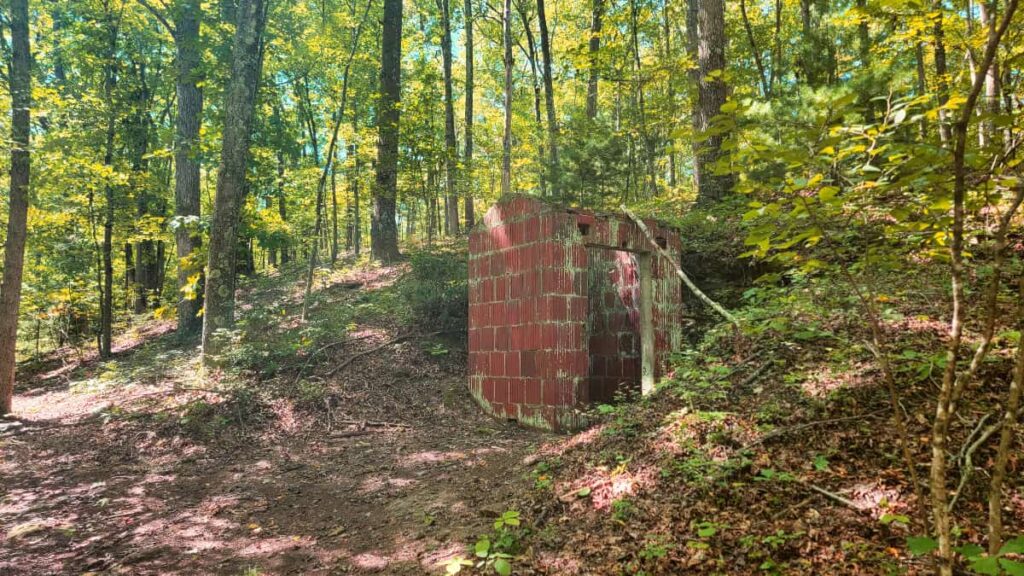 A red brick shed, no longer in use, stands off the side of a hiking trail