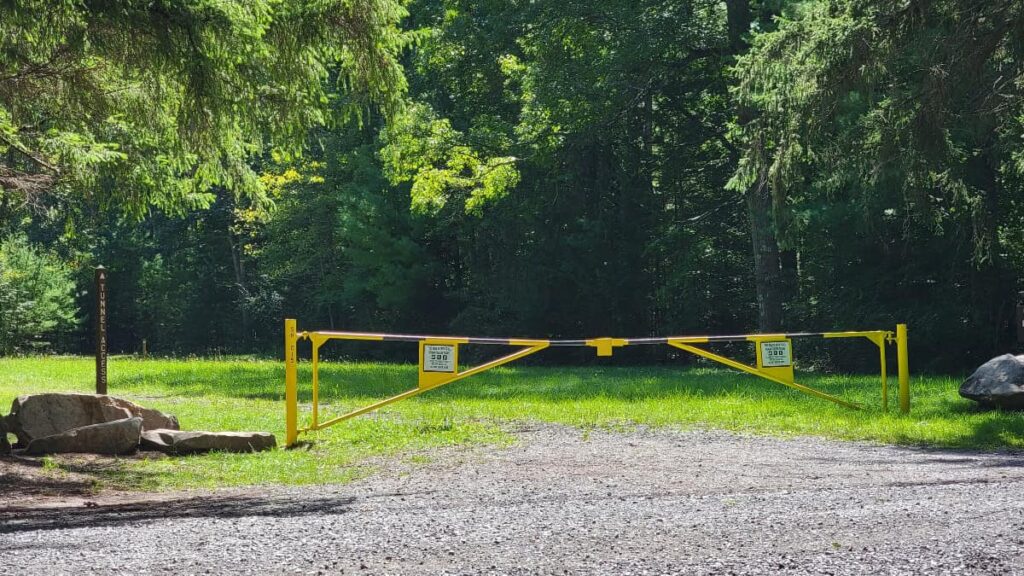 A yellow gate crosses over a gravel path to stop cars with a "tunnel access" sign to the left of the gate