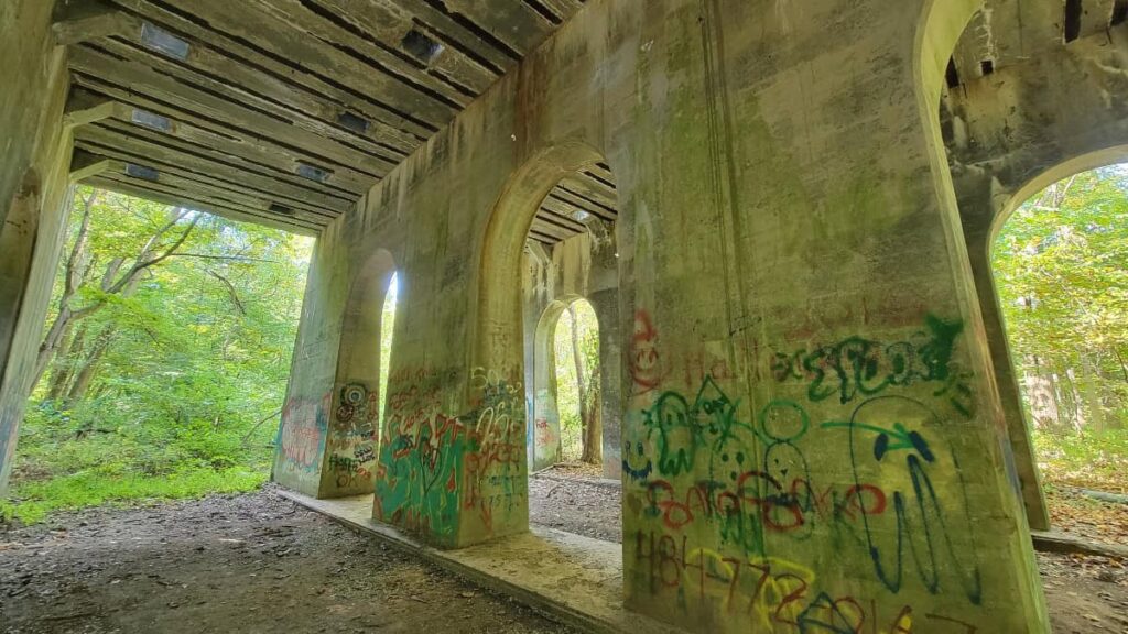 A concrete structure with graffiti and open arches stands in the woods at Monocacy Hill