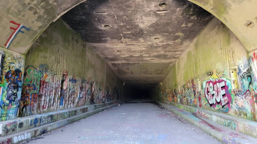 A view of an abadoned pa turnpike tunnel from just inside the entrance with lots of graffiti on the walls