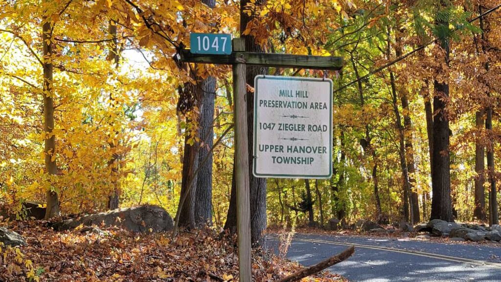 a white signs hangs from a wooden post with "mill hill preservation area"