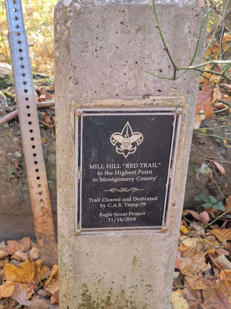 sign on stone marker reads "Mill Hill red Trail to Highest point in Montgomery County"