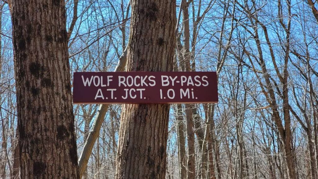 a sign hangs on a tree and reads "wolf rocks bypass at jct 1.0 mi"