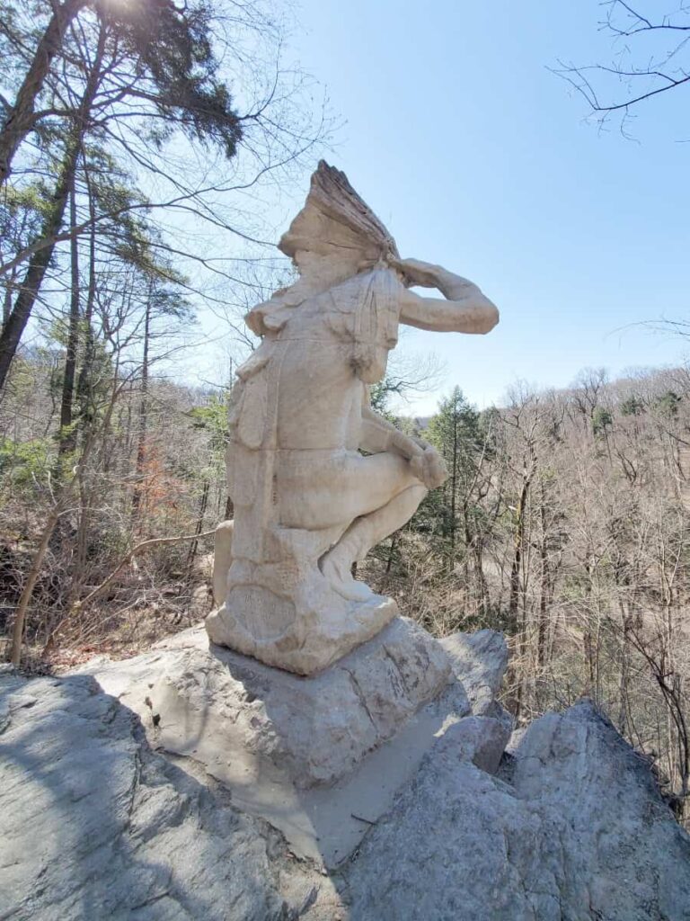 A marble statue depicts a Native American looking over over the gorge at Wissahickon