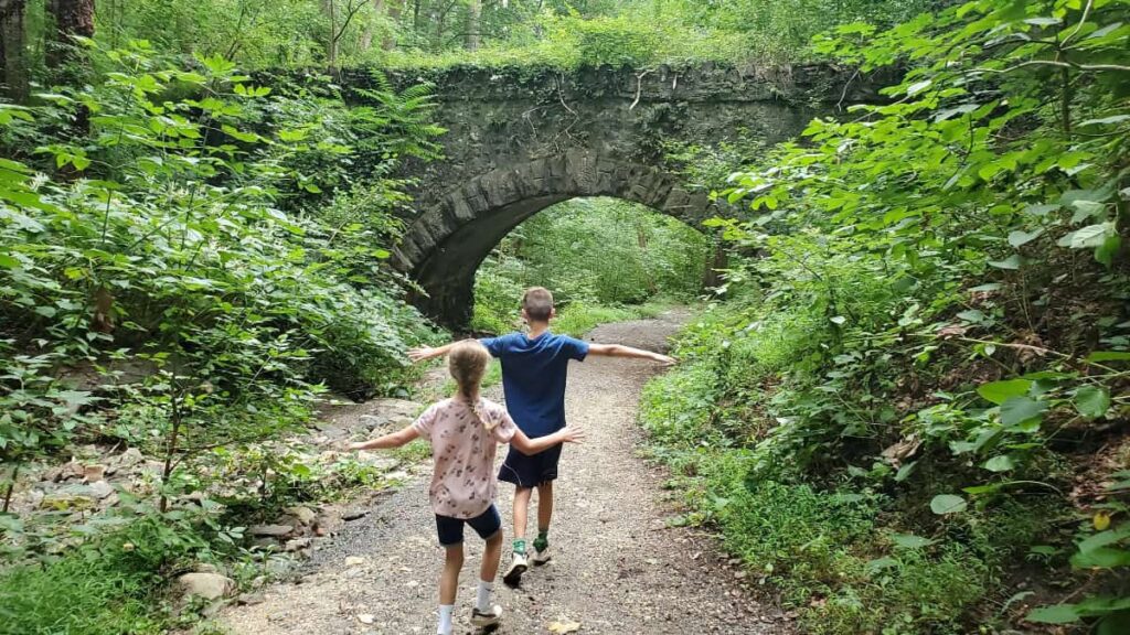 two kids run along a trail that passes under a stone archway