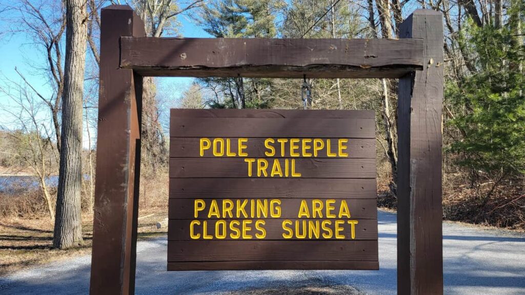 A wooden sign reads " Pole Steeple Trail: Parking area closes at sunset"