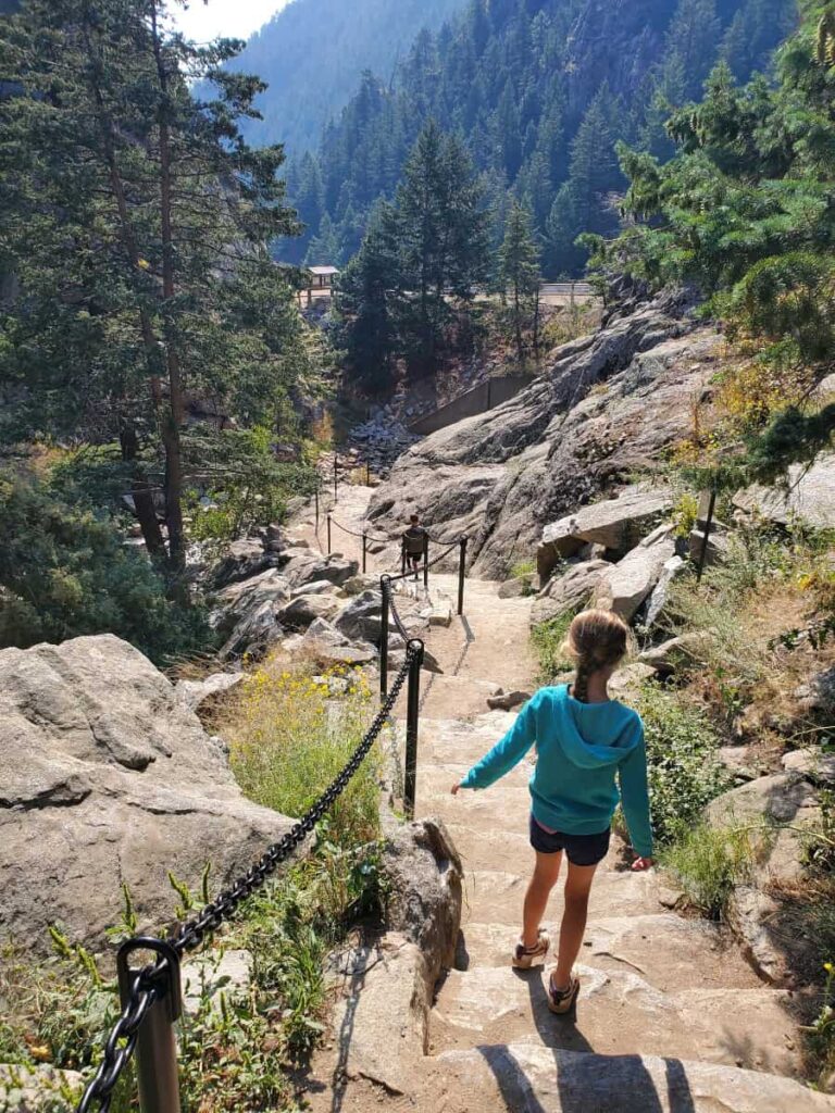 A young girl walks down stone steps next to a chain barrier with the Boulder Canyon in the distance