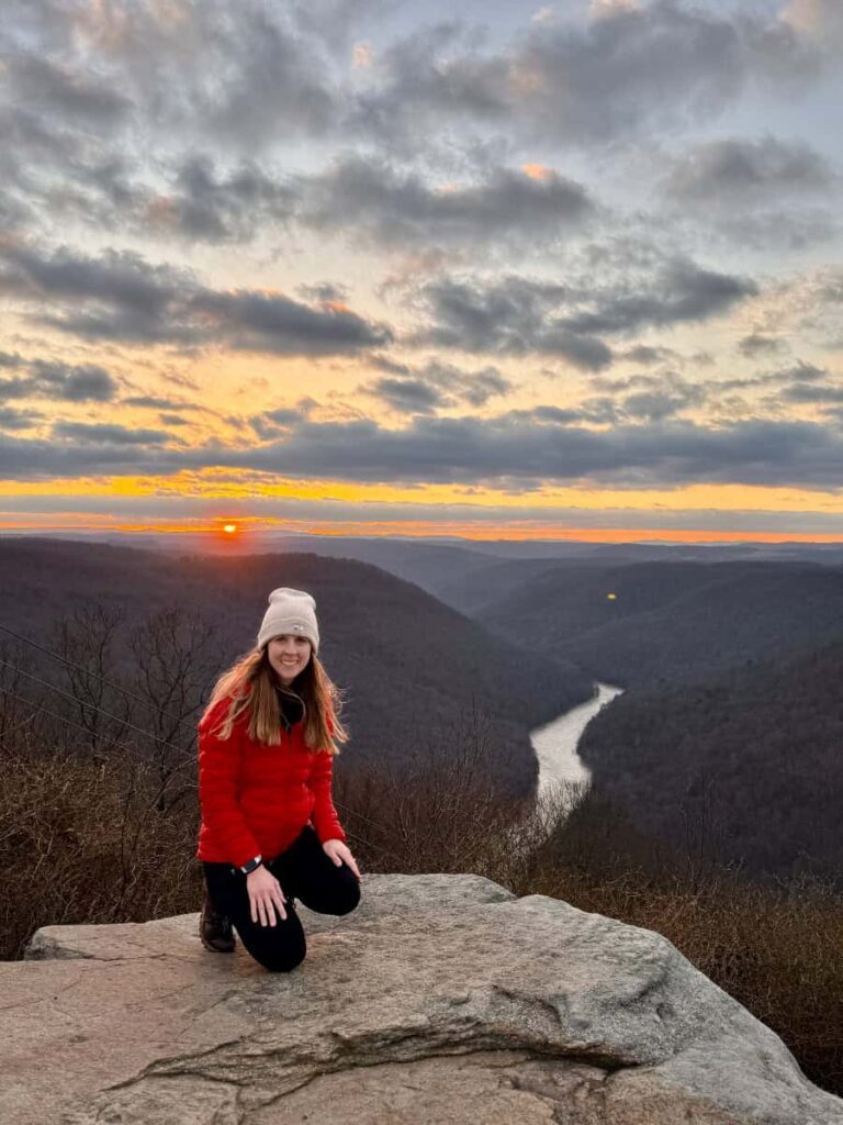 A woman kneels on a rock overlooking at river at sunrise