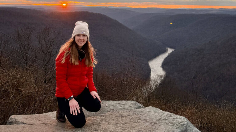 A woman kneels on a rock overlooking at river at sunrise