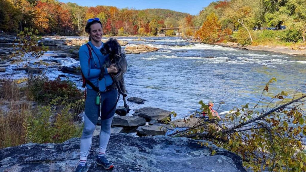 A woman hold her dog while standing next to the Youghiogheny River