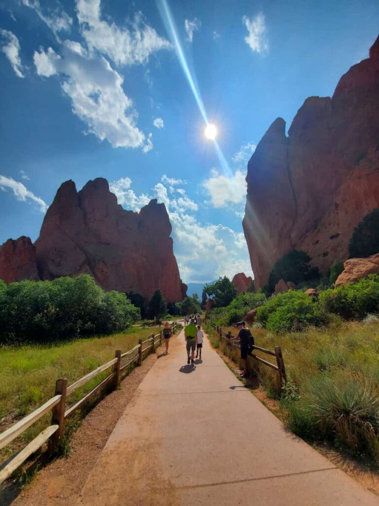 People walk along a flat paved path in Garden of the Gods with large rock formations in the distance