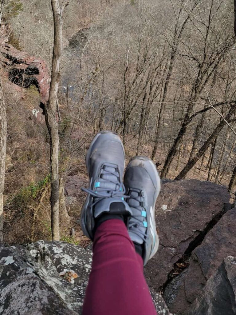 Feet are crossed showing off hiking boots with trees in the distance
