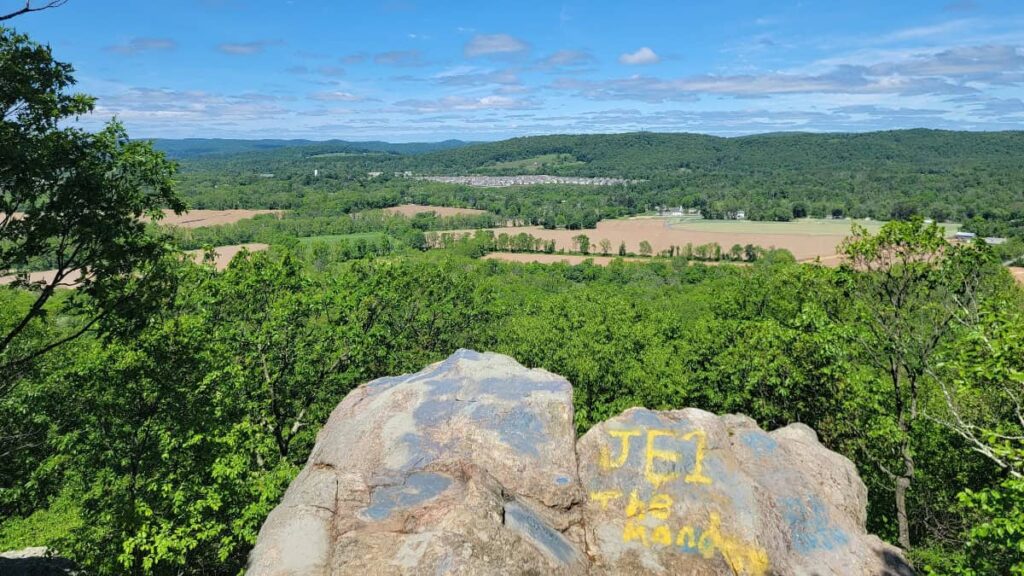 View looking past a rock outcropping towards farm land and mountains in the distance