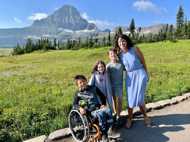 A mother a three kids (one is seated in a wheelchair) stand on a path with a mountain in the background