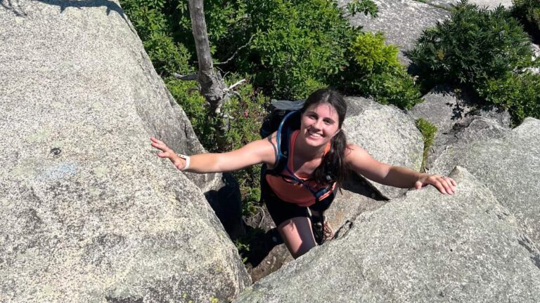 A woman smiles as she scrambles up large rocks