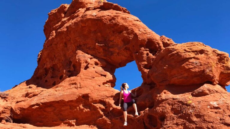 a woman sits inside a red rock arch