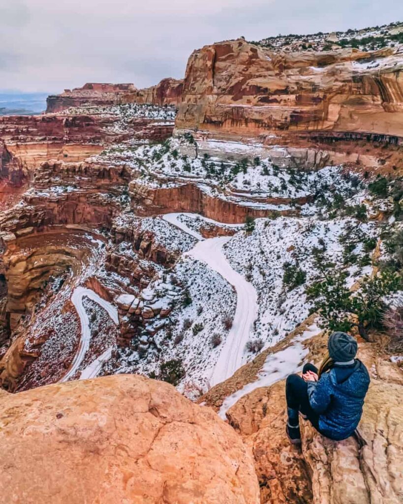 a women sits overlooking a red rock canyon with light snow