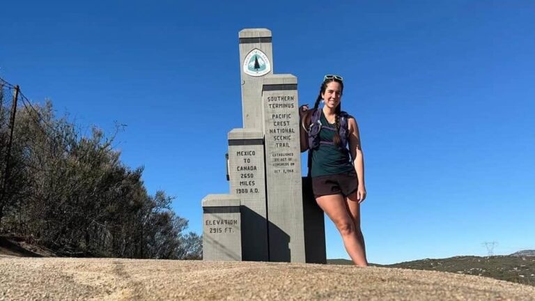 A woman stands next to a stone marker on the PCT